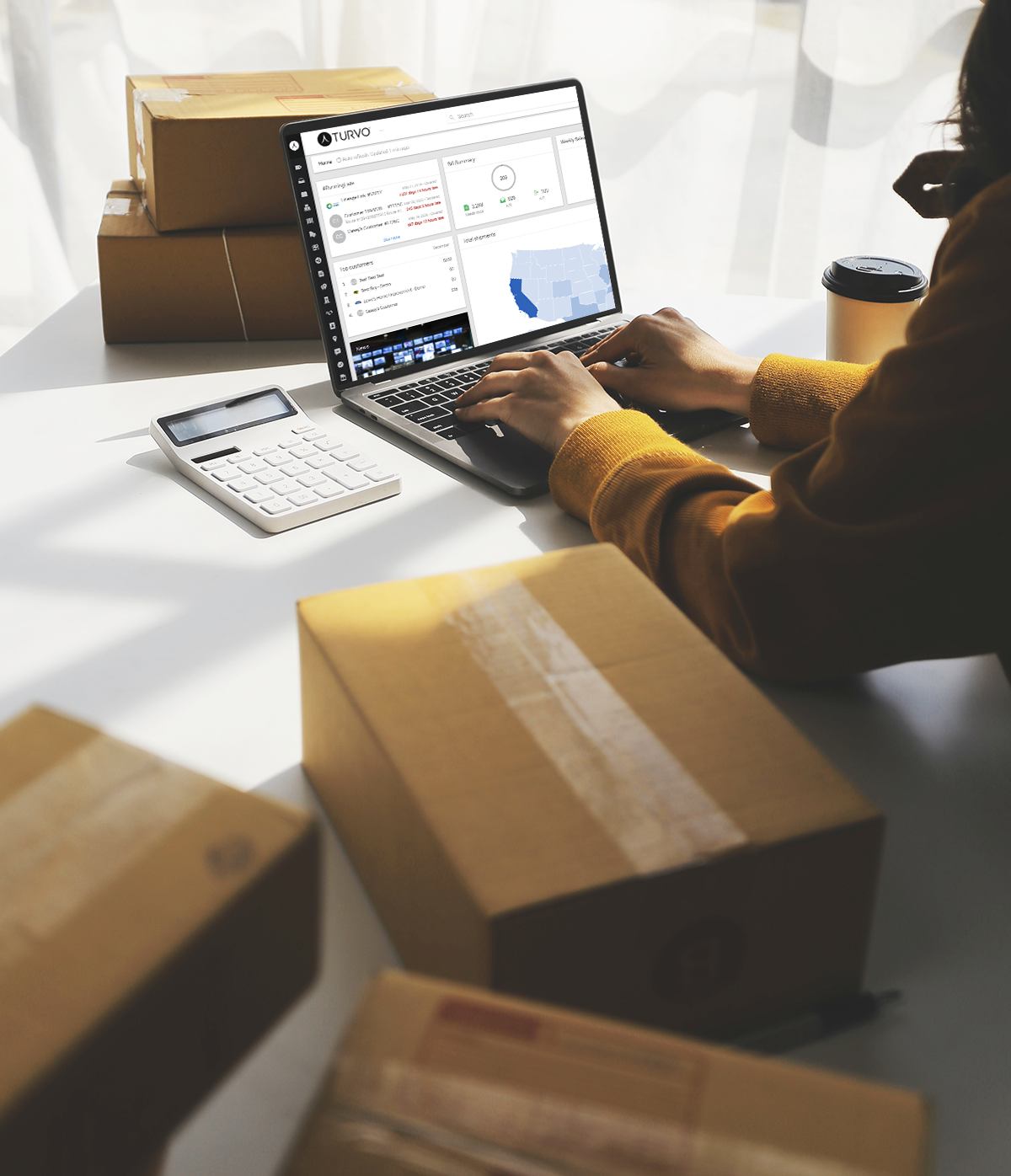 A woman on the laptop in a warehouse facility moving boxes. A man with a clipboard making a list of inventory.